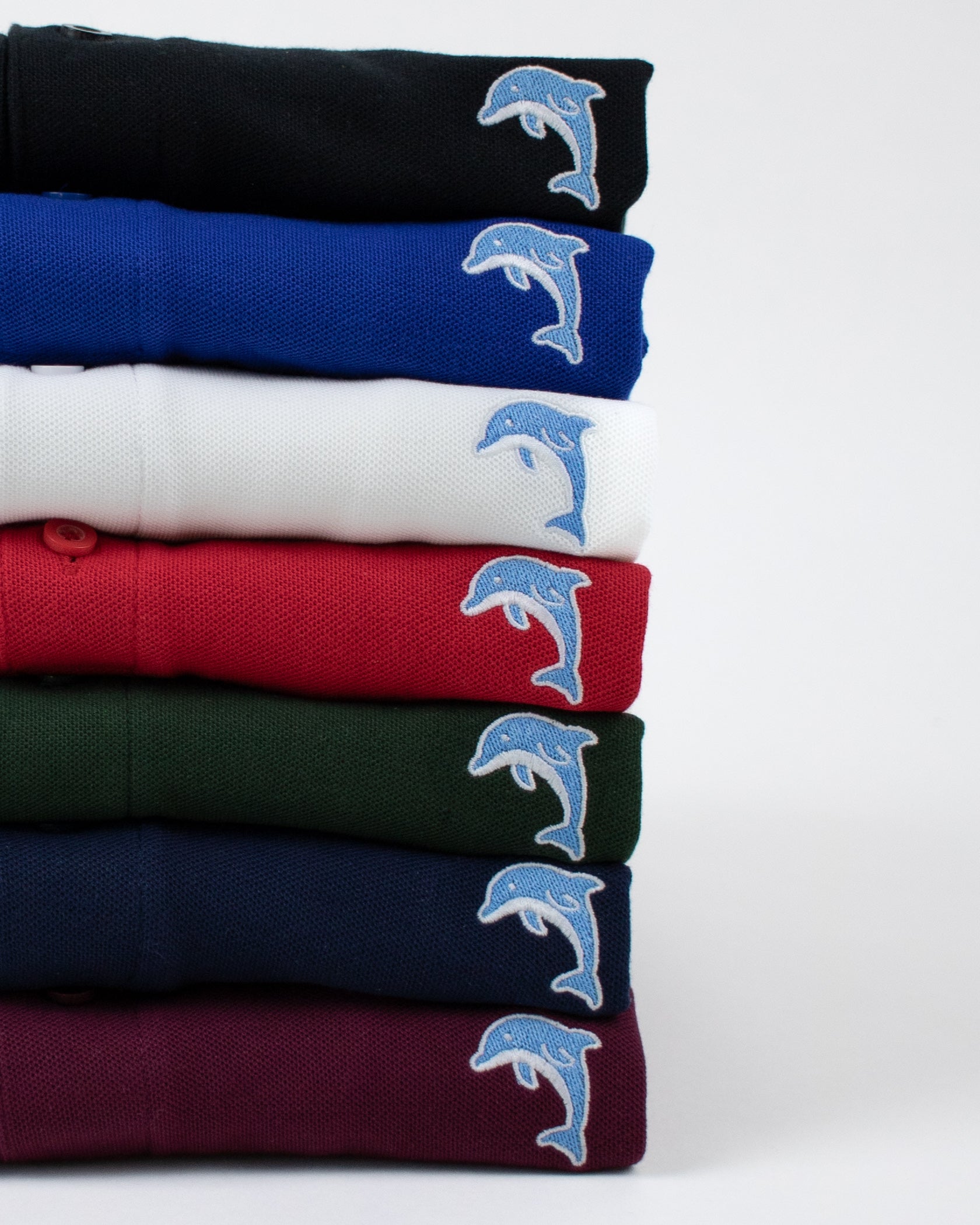 Stack of folded polo shirts with dolphin designs on a white background