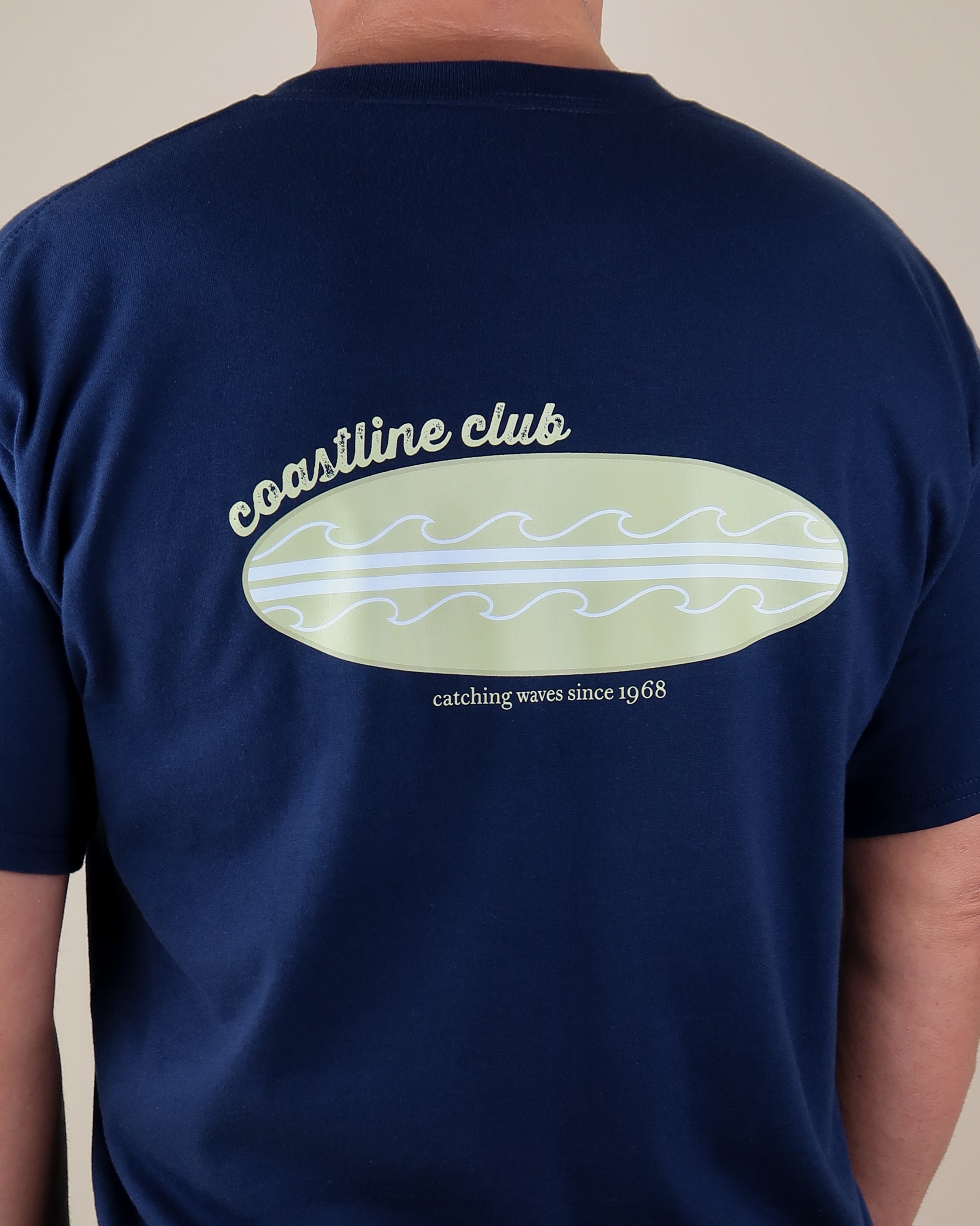 Navy blue t-shirt with 'coastline club' surfboard design on the back against a neutral background