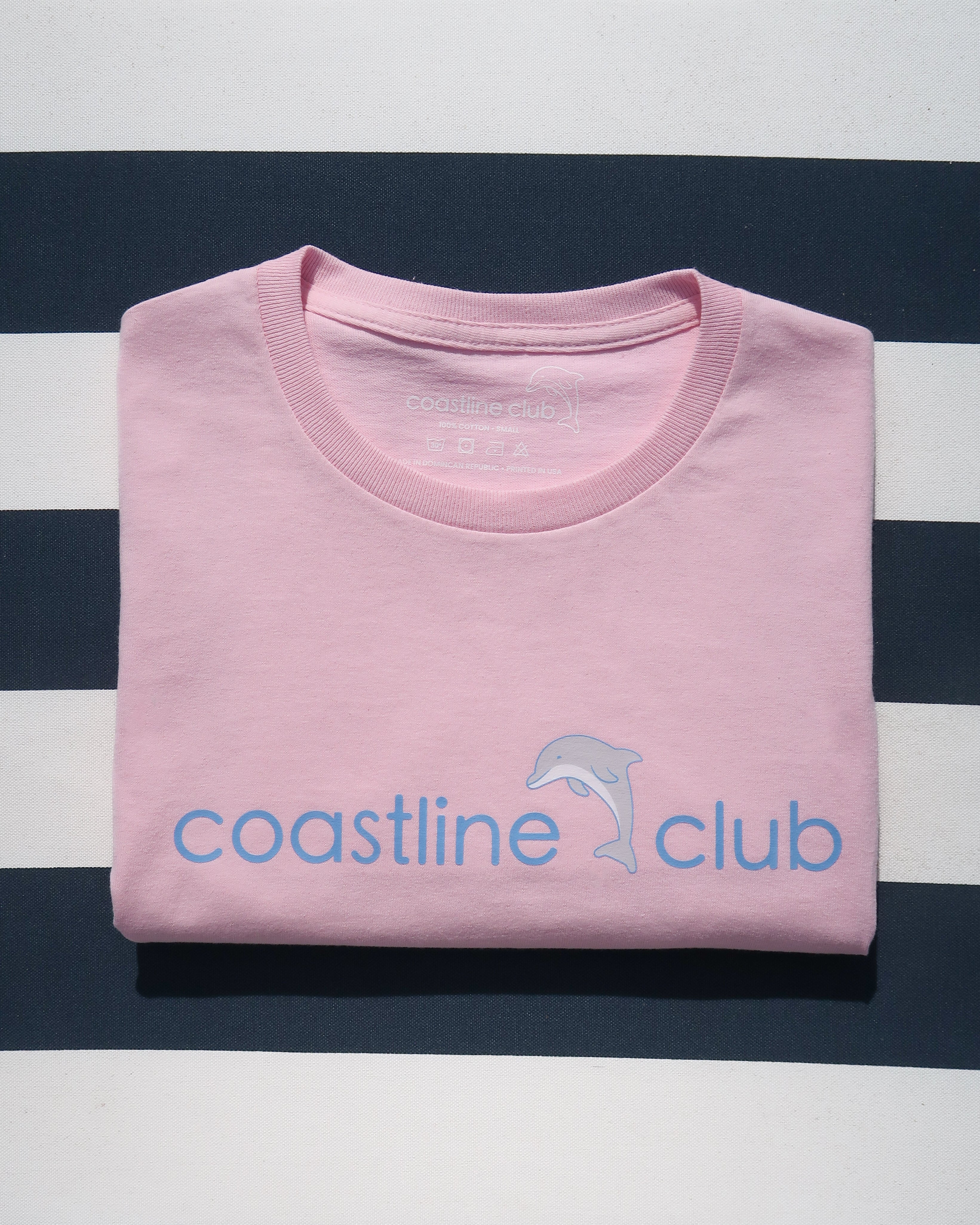 Folded light pink shirt with blue dolphin coastline club logo on a striped background
