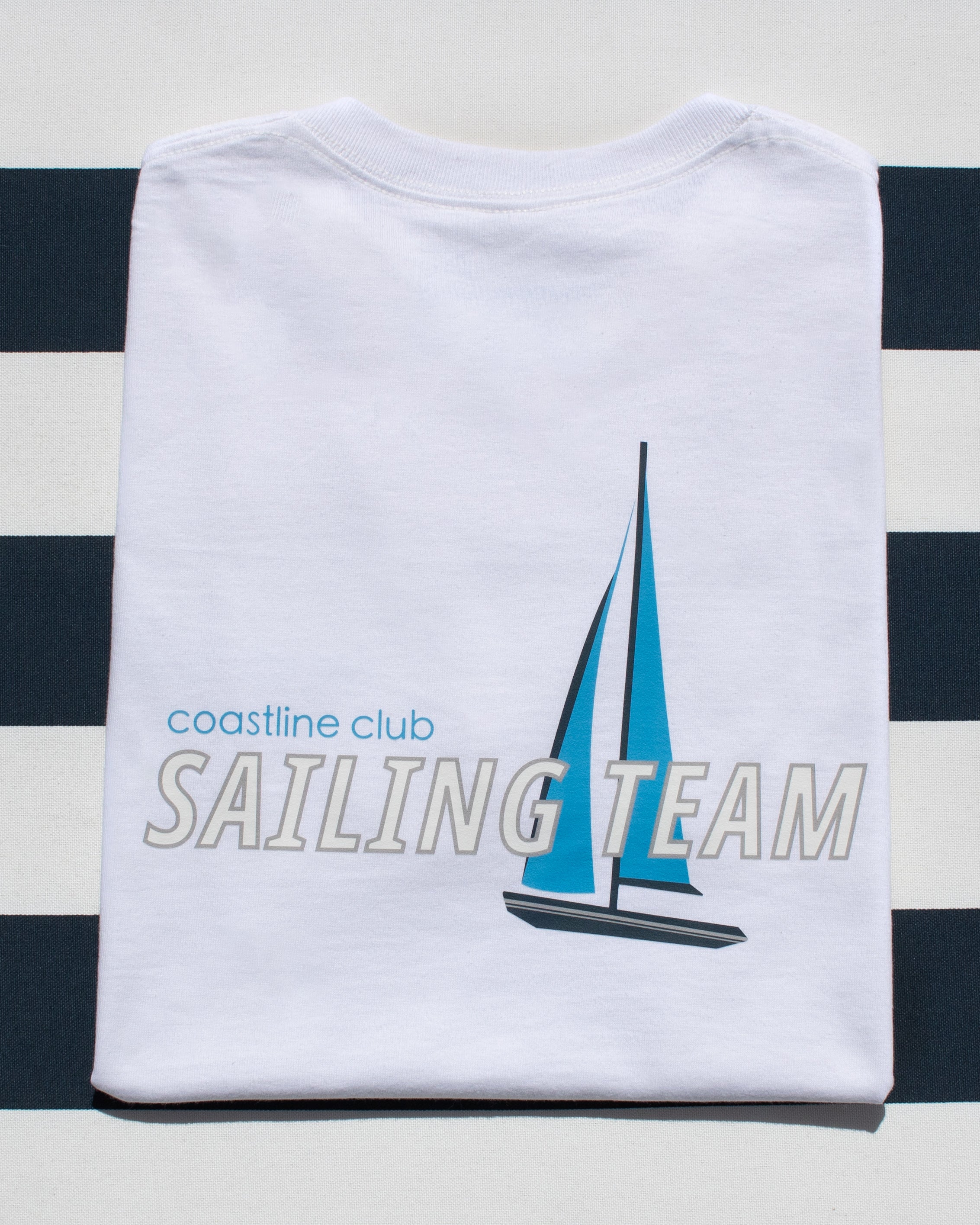 White t-shirt with sailboat graphic and 'coastline club SAILING TEAM' text on a striped background