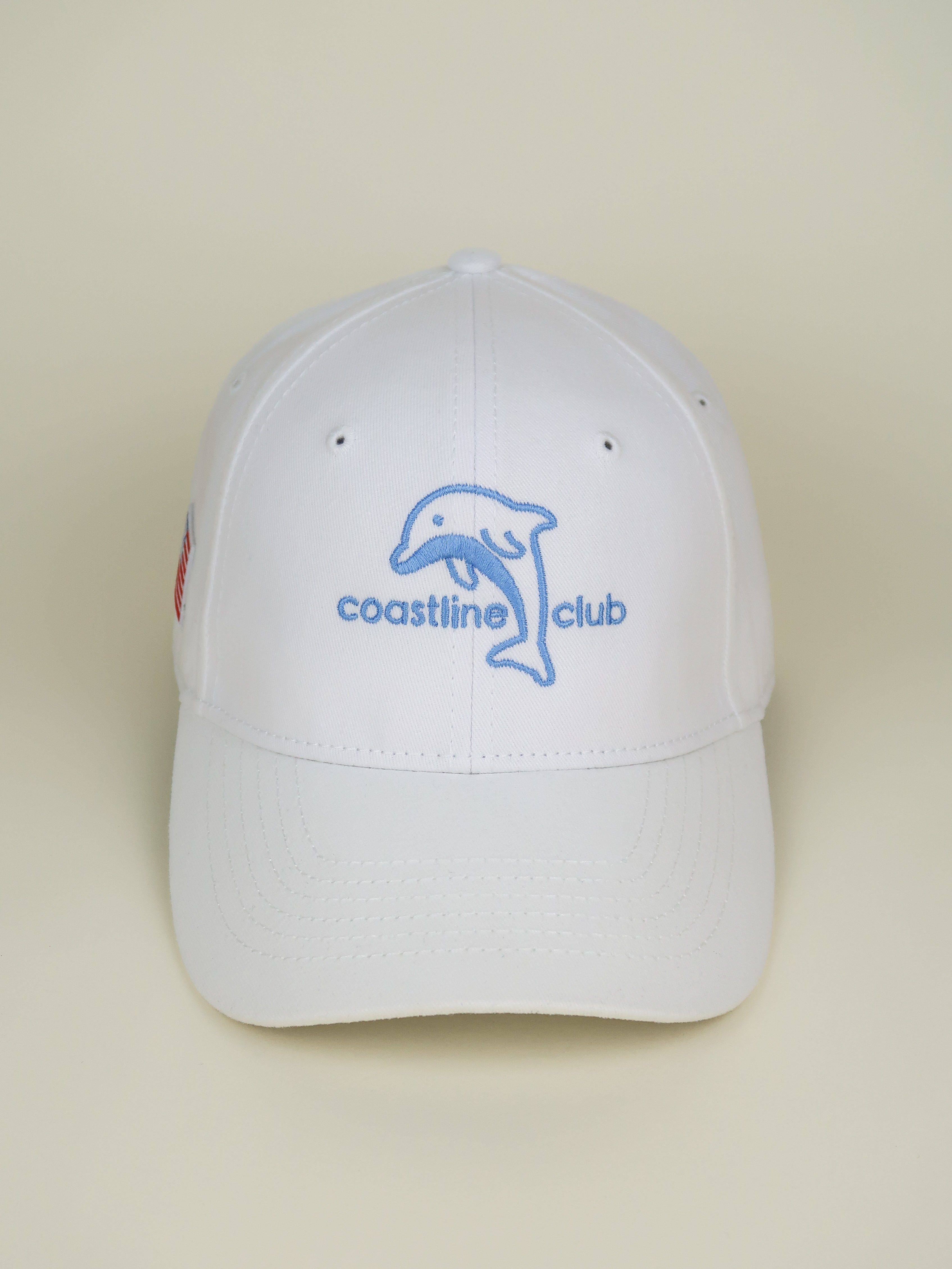 White cap with 'coastline club' logo on a beige background