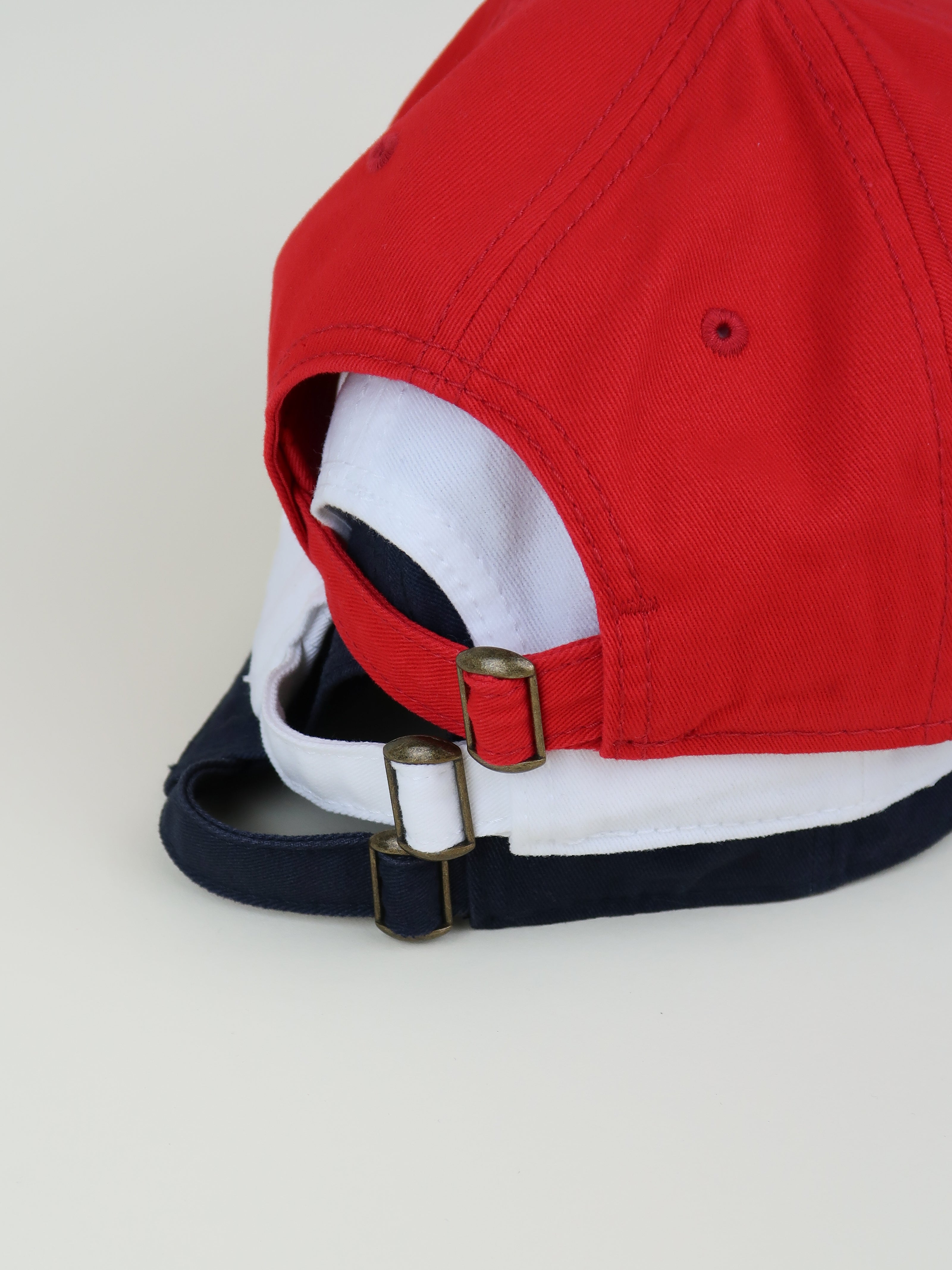 Close-up of a red cap with a white interior and Navy strap on a light gray background