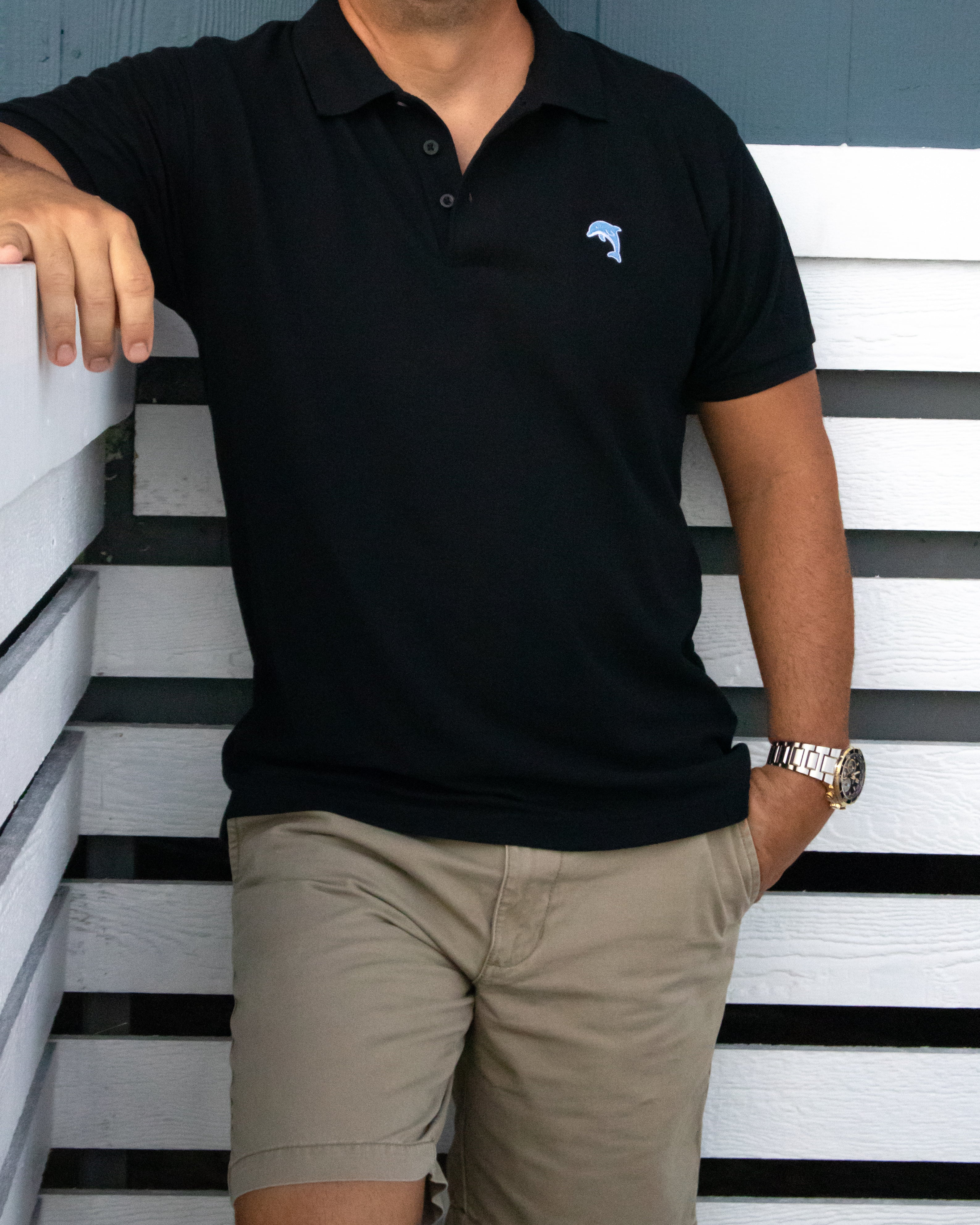 Person wearing a black polo shirt with a dolphin logo on a striped background