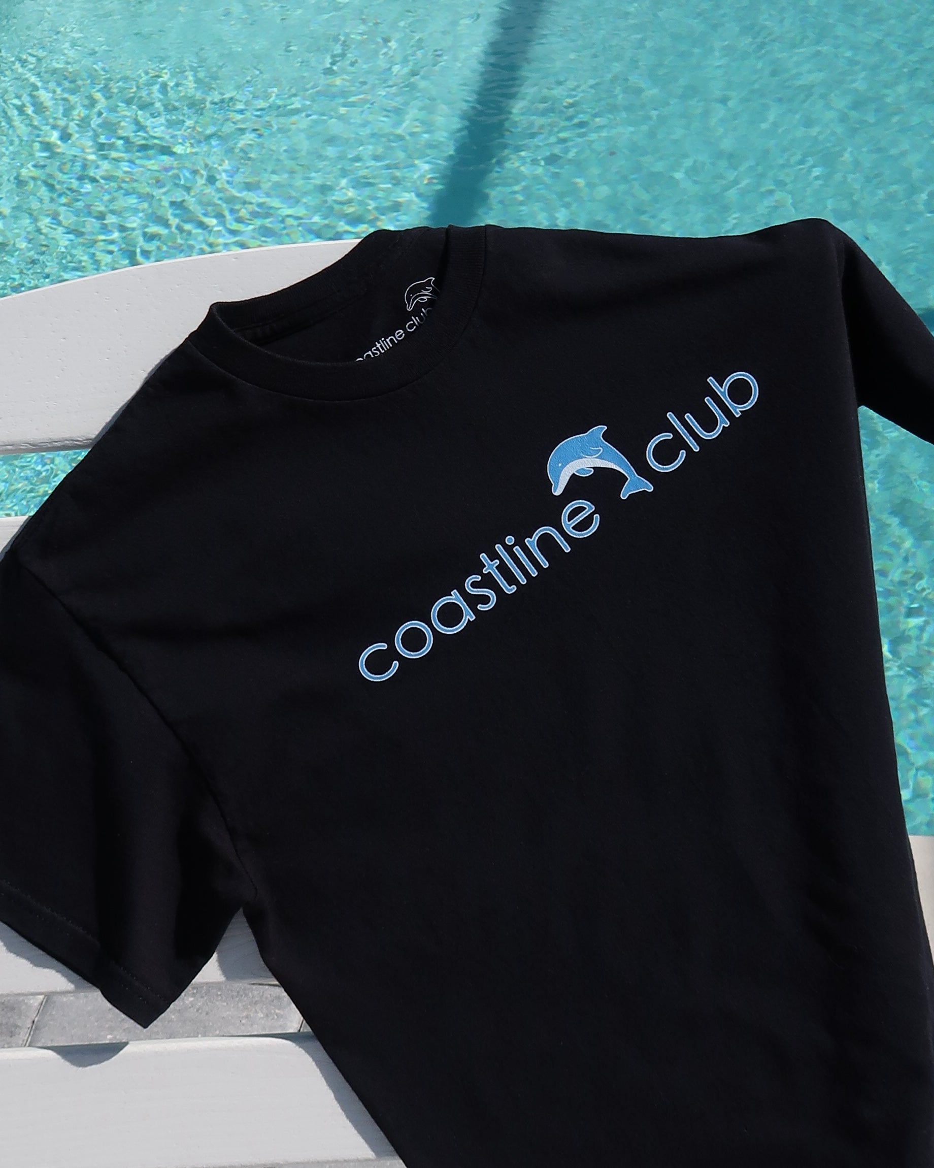 Black t-shirt with 'coastline club' logo on a poolside background