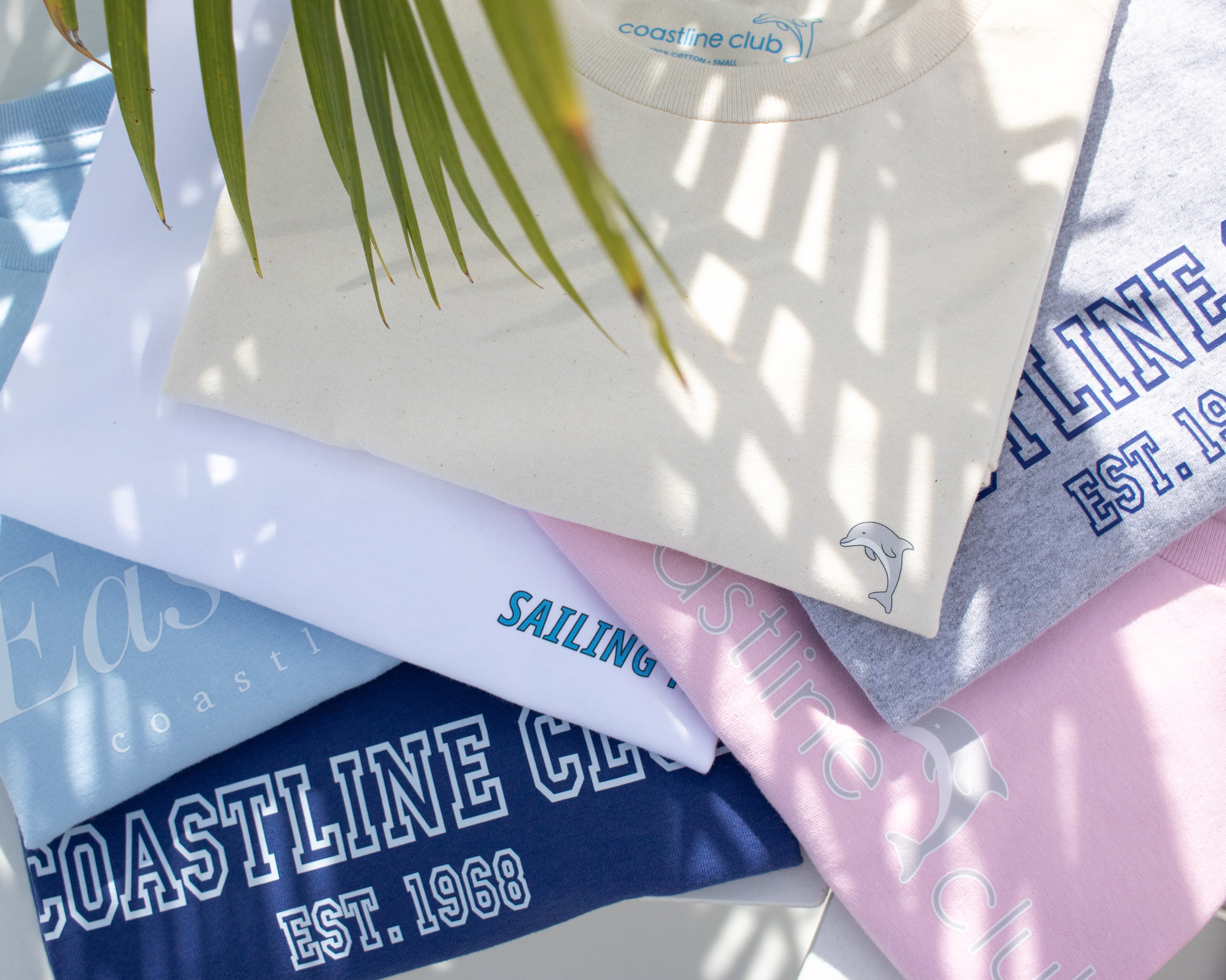 Stack of colorful t-shirts with text and branding on a light background