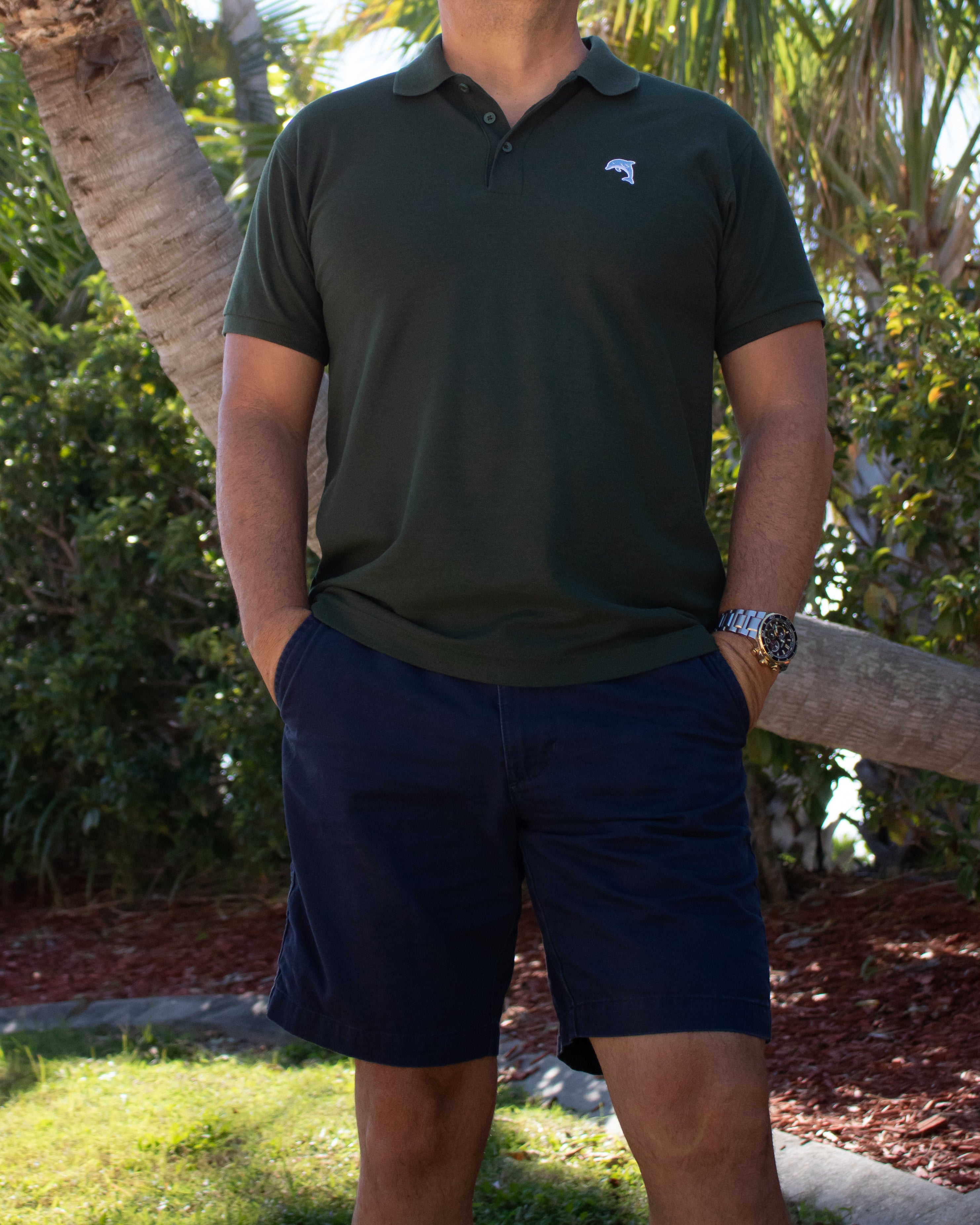 Person wearing a green polo shirt with a dolphin logo, standing outdoors with trees in the background