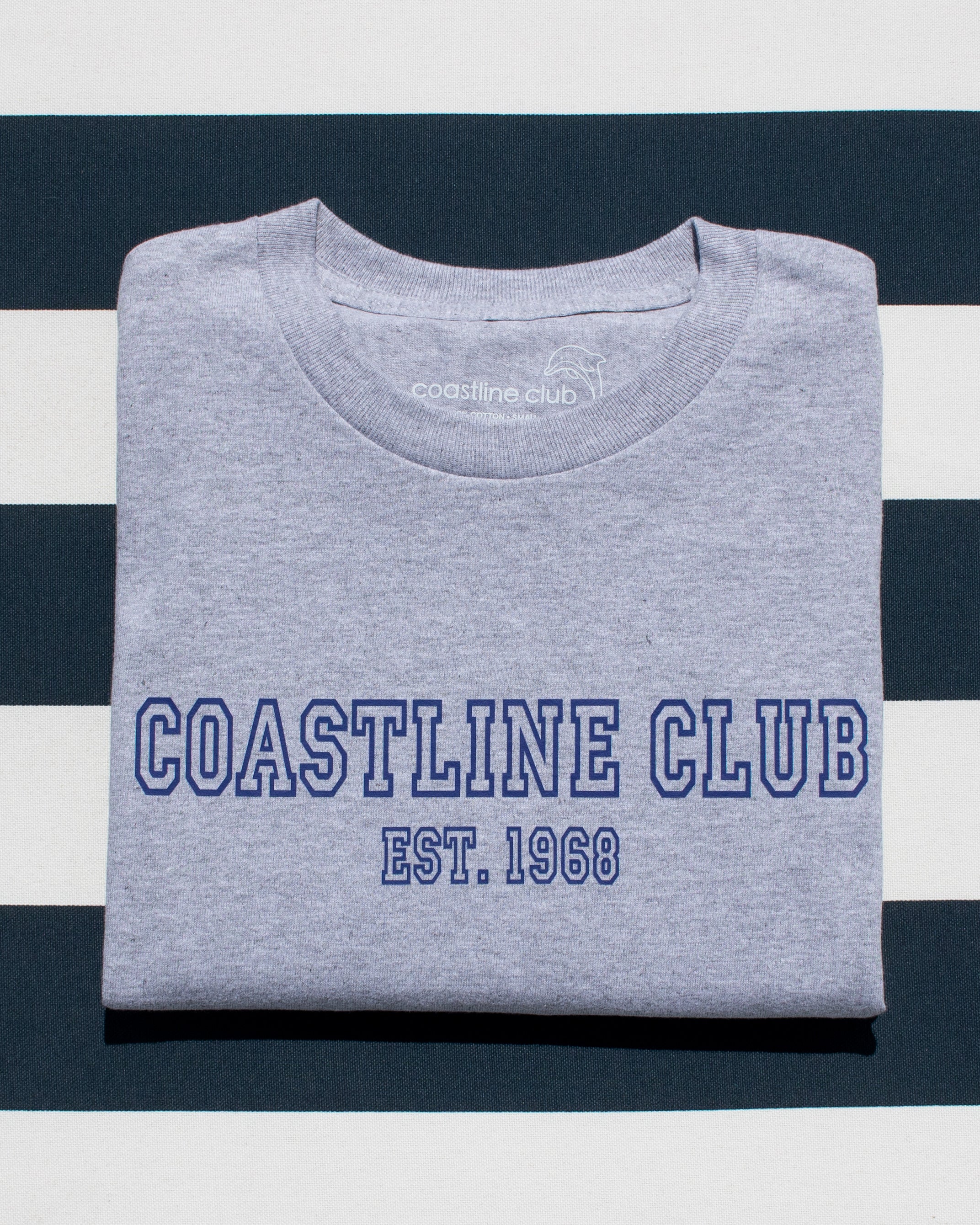 Folded gray t-shirt with 'Coastline Club' text on a striped background