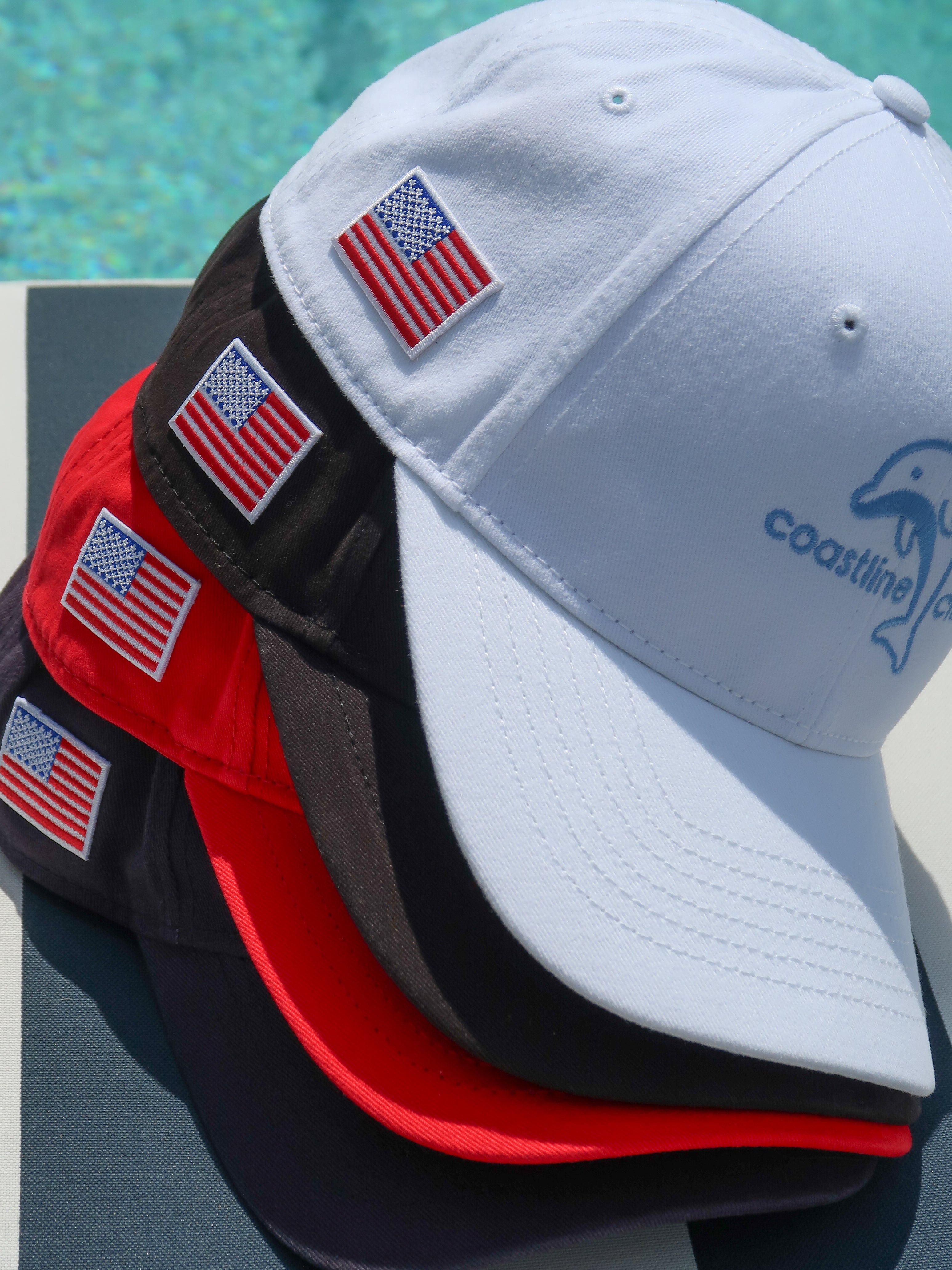 Four baseball caps with American flags and a logo on a poolside background