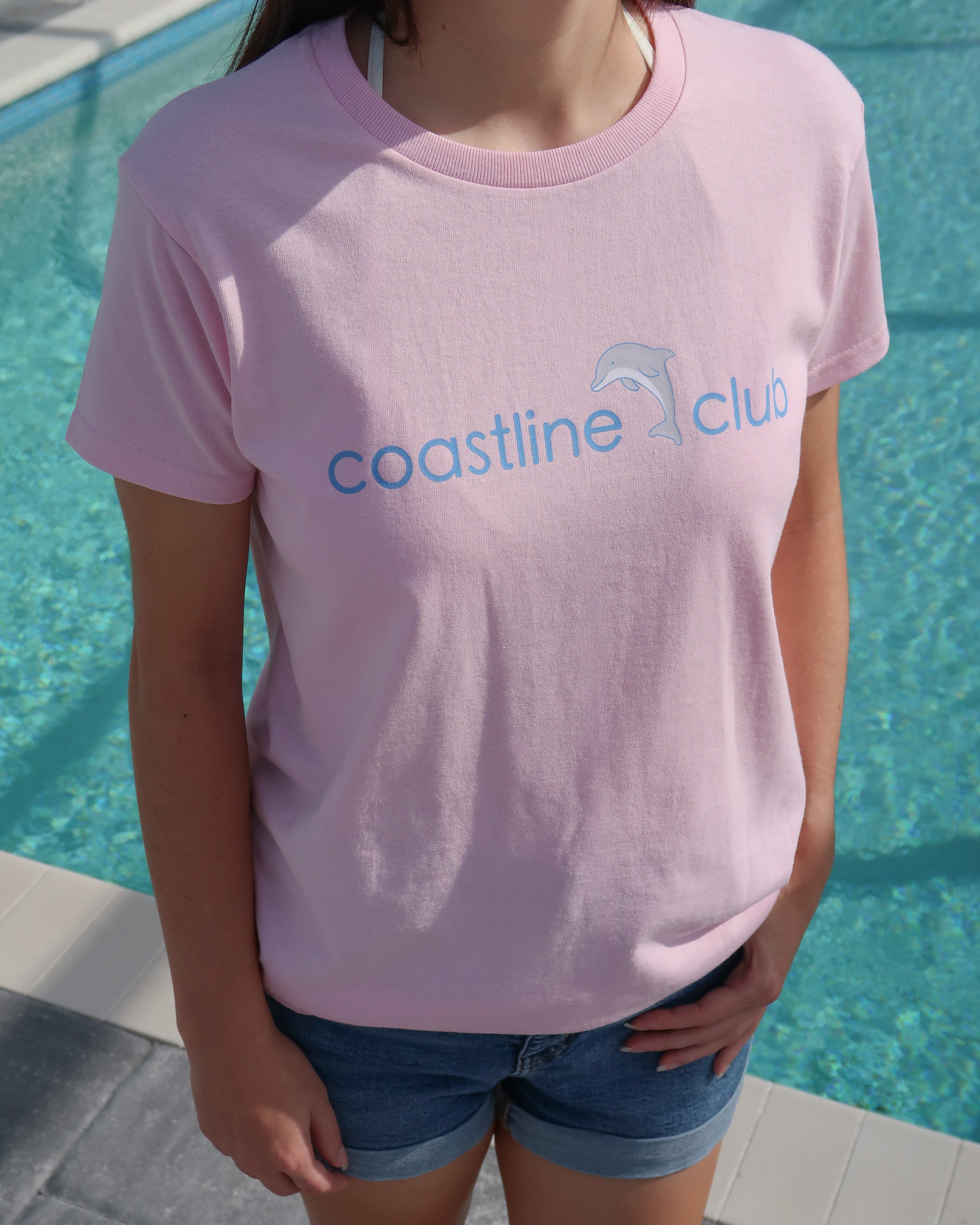 Person wearing a pink 'coastline club' t-shirt by a pool