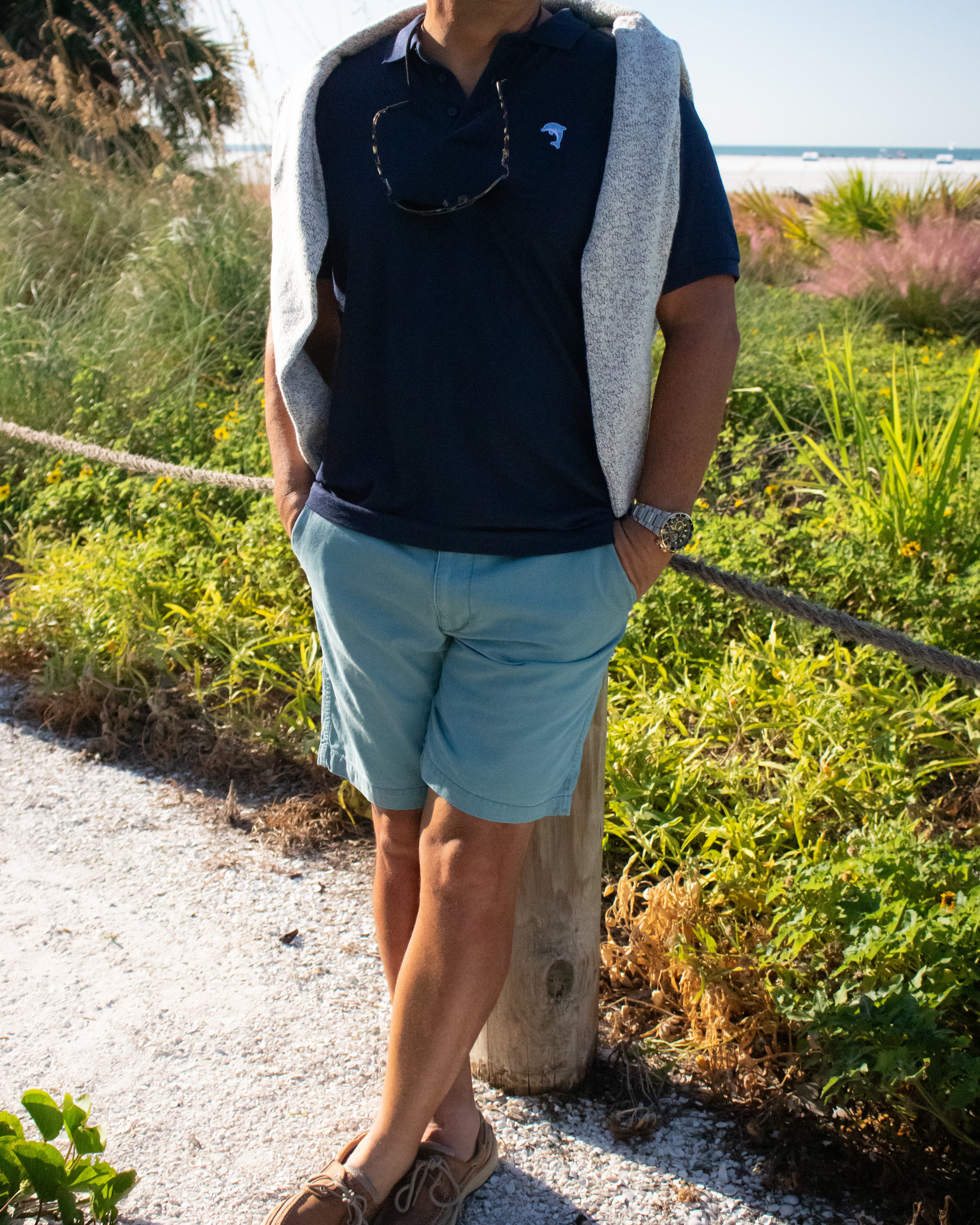 Person standing outdoors by a grassy area with a beach background