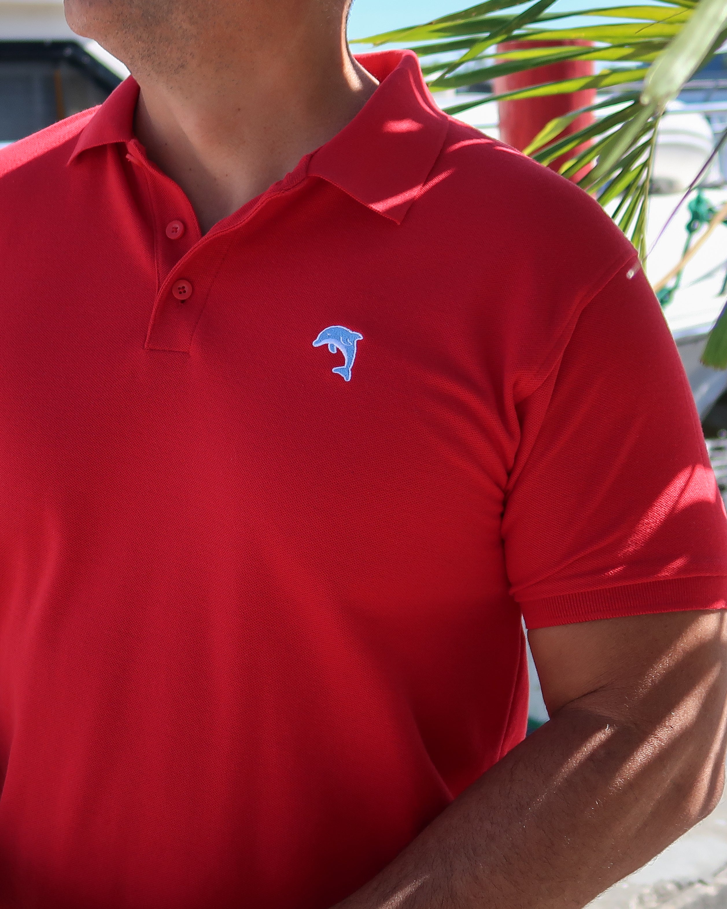 Red polo shirt with a dolphin logo worn by a person, with a marina background.