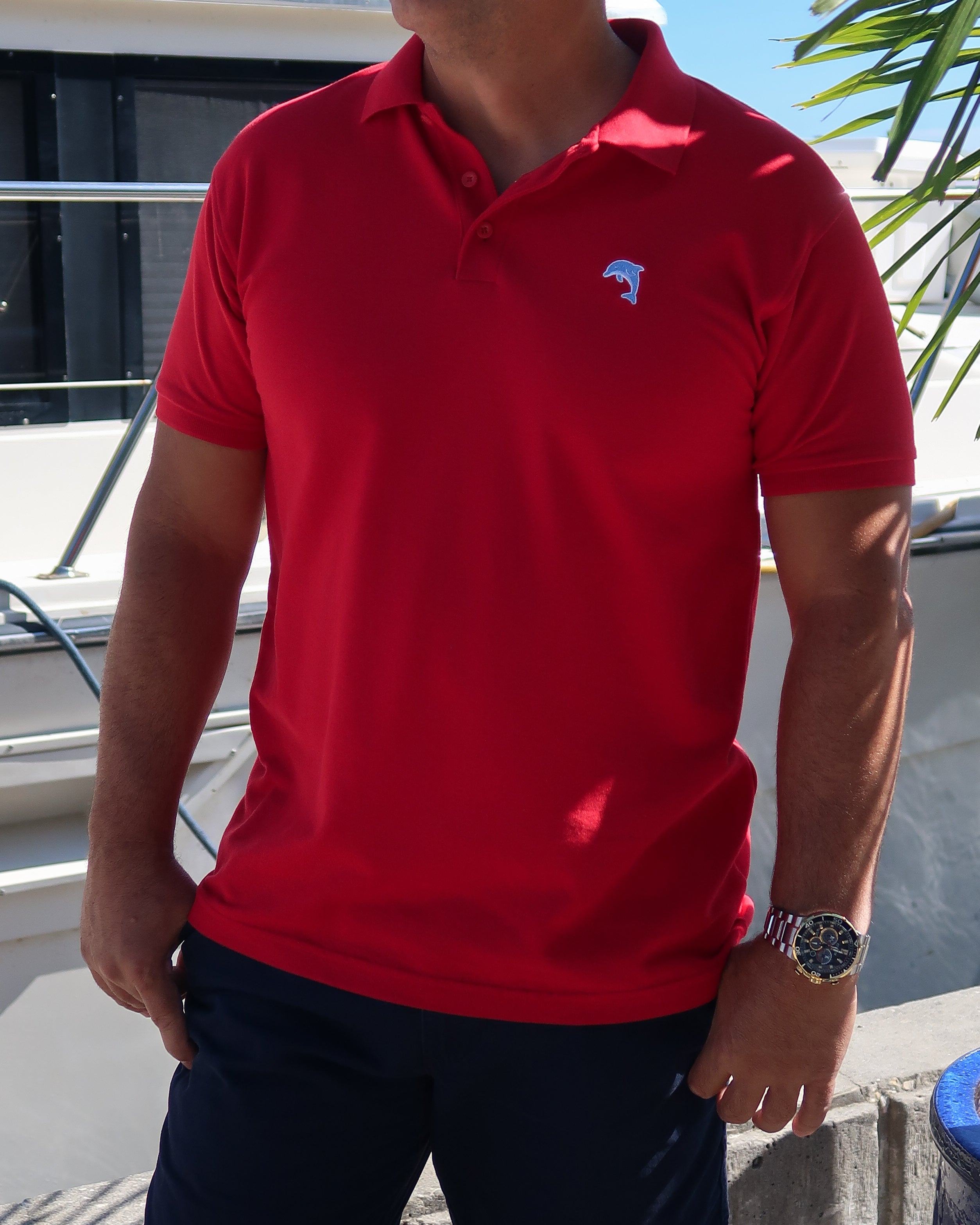 Person wearing a red polo shirt with a dolphin logo, standing in front of a boat.