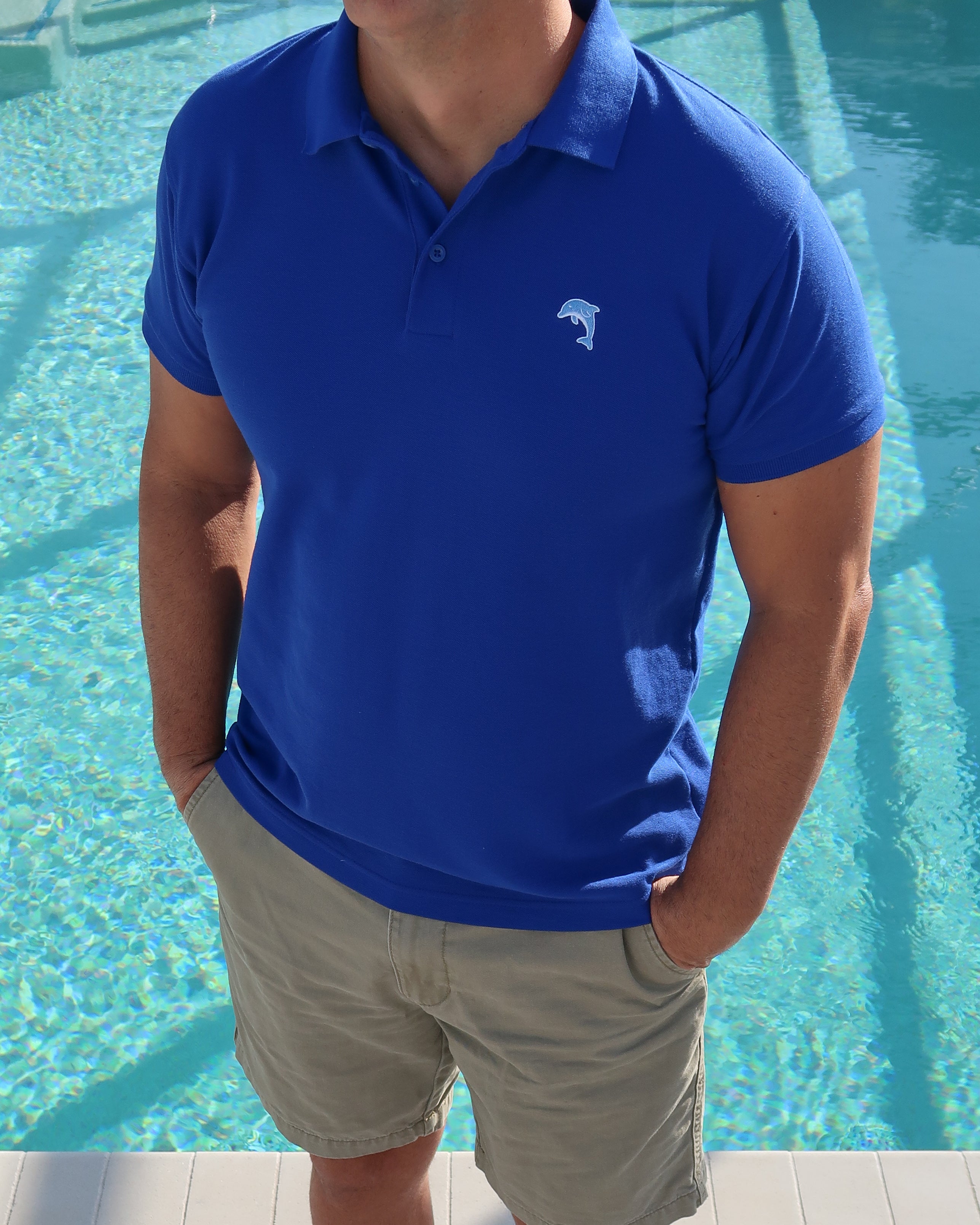 Person wearing a royal blue polo shirt with a Dolphin logo by a pool