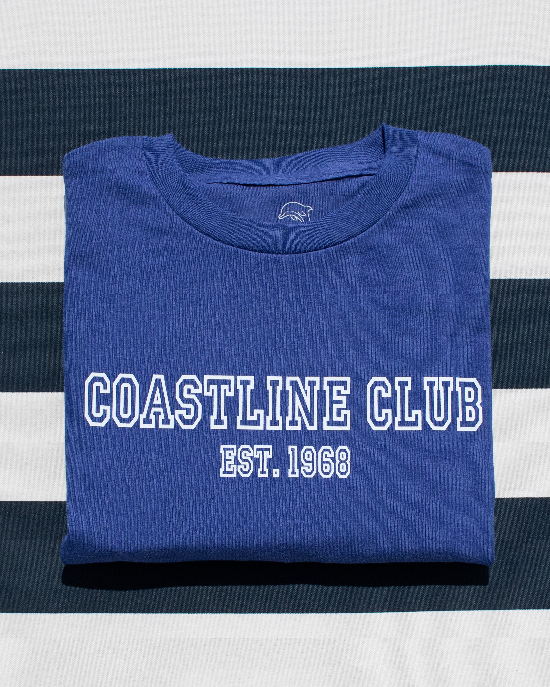 Folded blue t-shirt with 'Coastline Club Est. 1968' text on a striped background