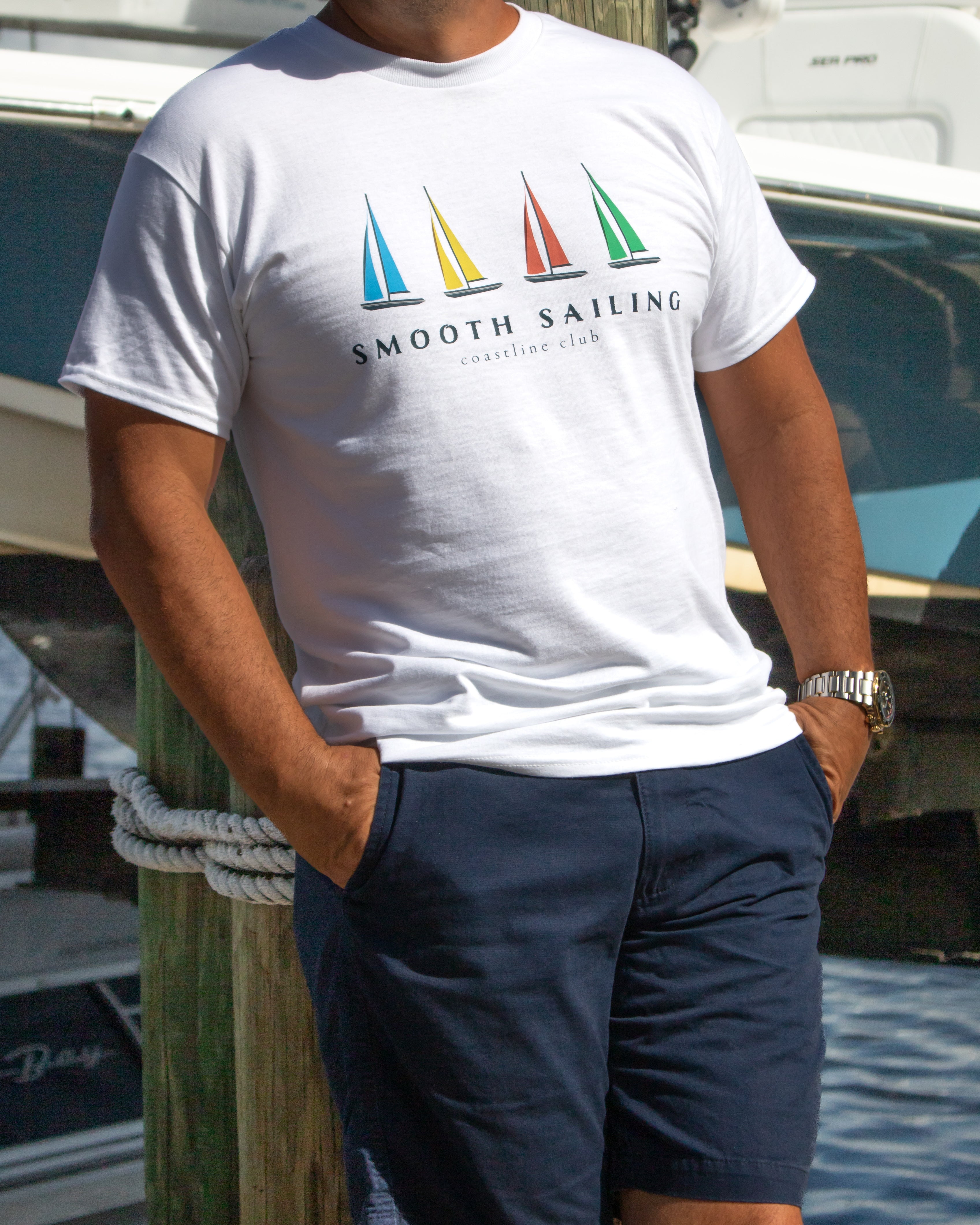 Person wearing a white t-shirt with 'Smooth Sailing' graphic, standing by a dock.