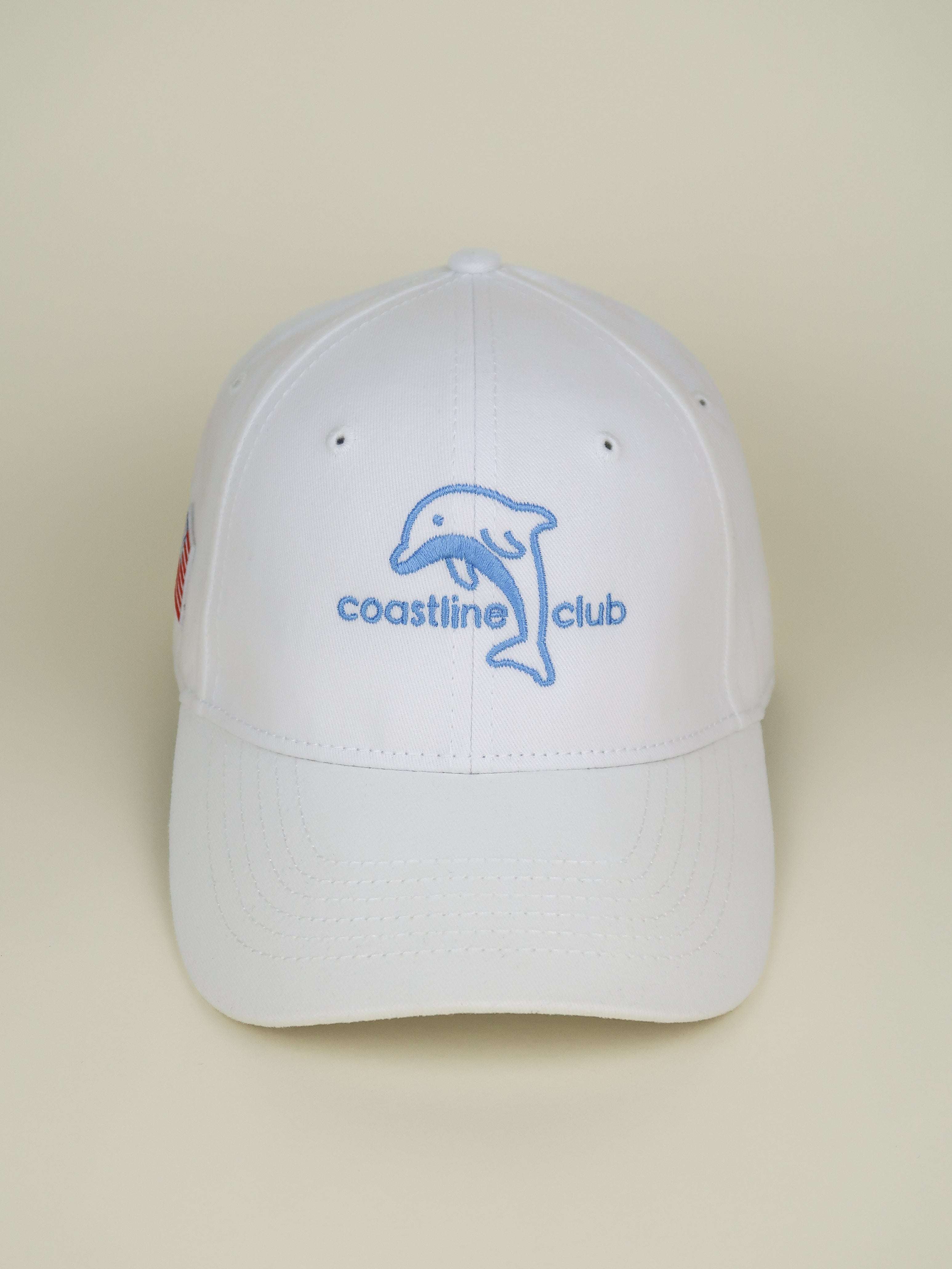 White cap with 'coastline club' logo on a beige background