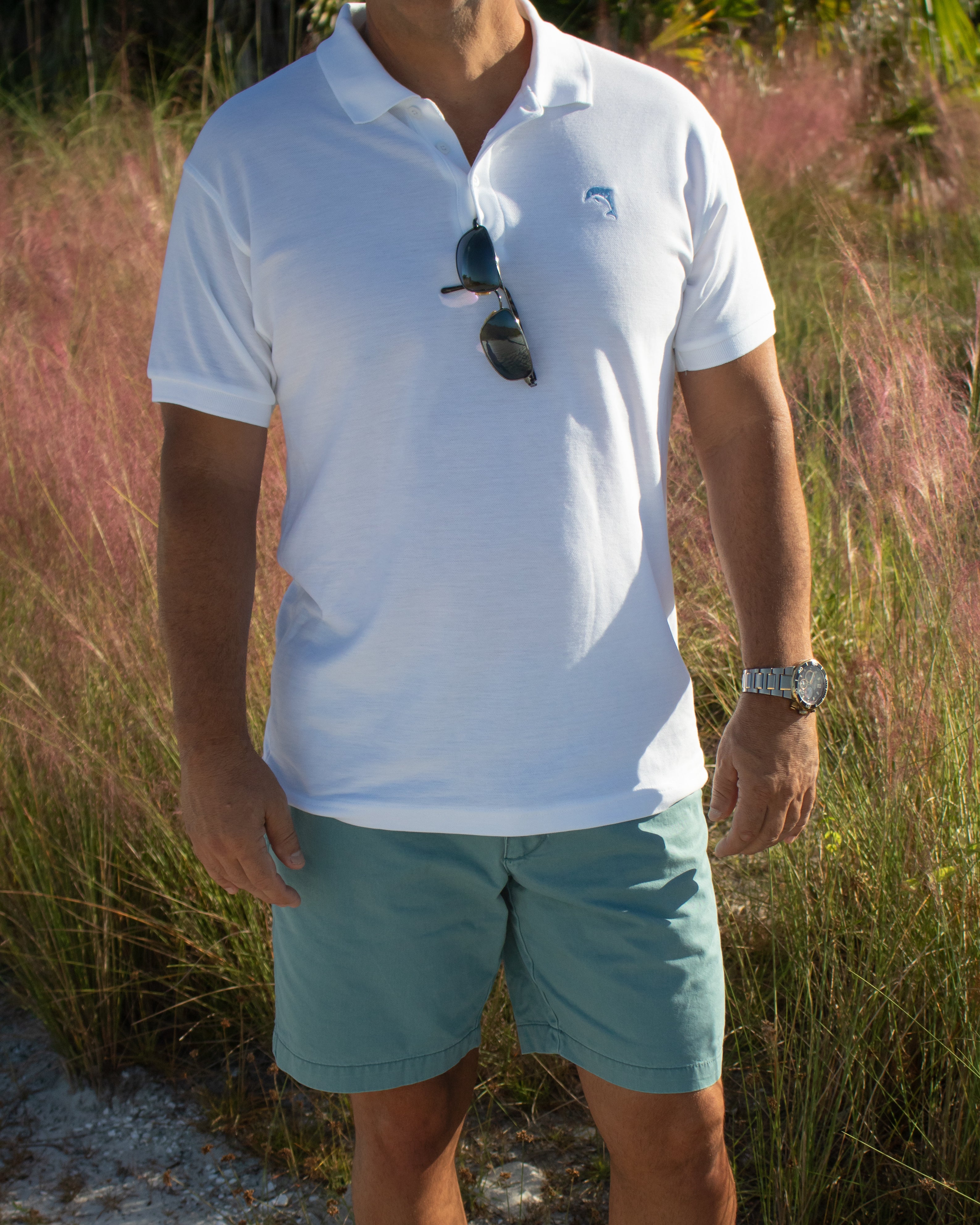 Person wearing a white polo shirt and light blue shorts standing in a natural setting.