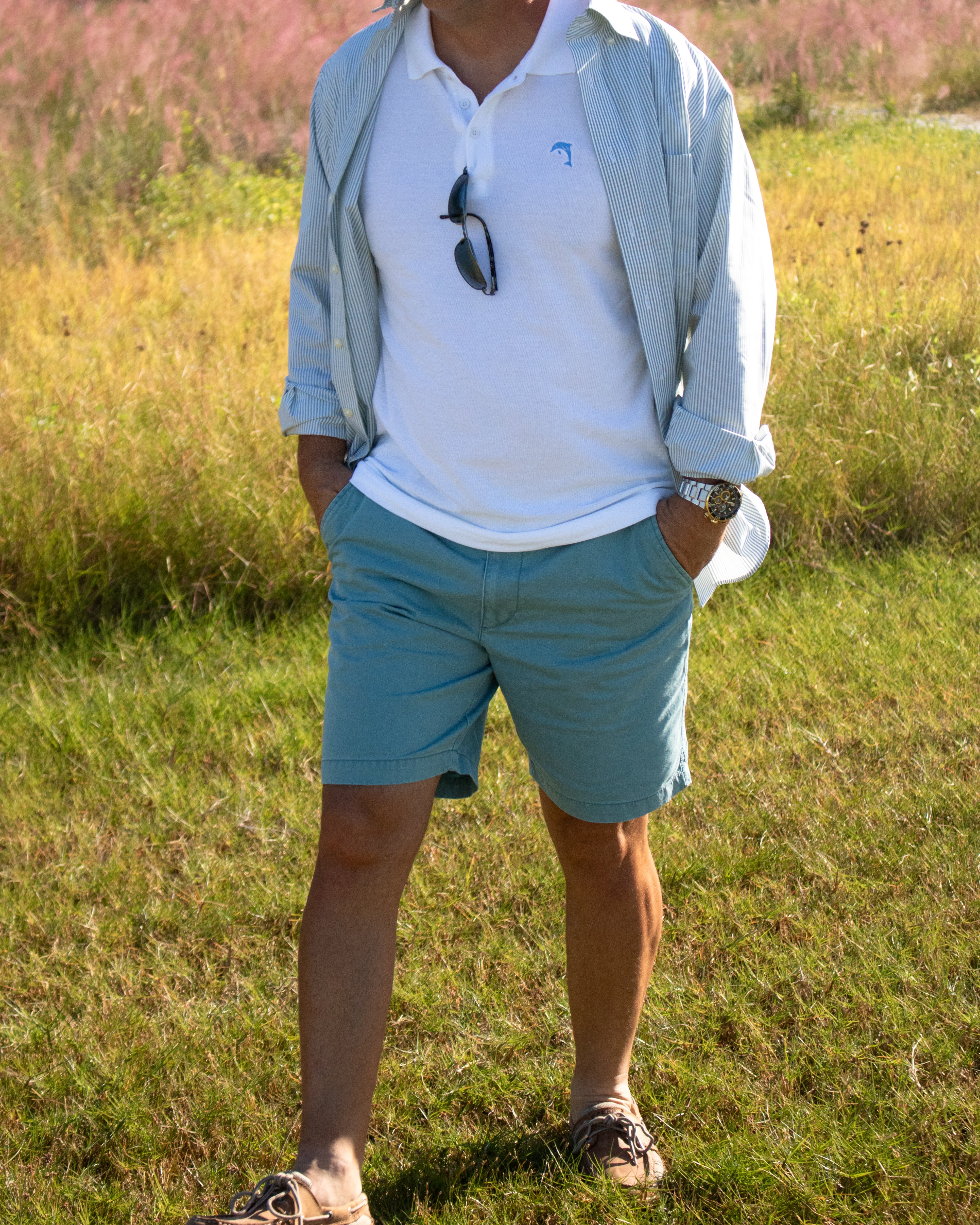 Person wearing a light blue shirt, white polo shirt, and teal shorts standing in a grassy field.