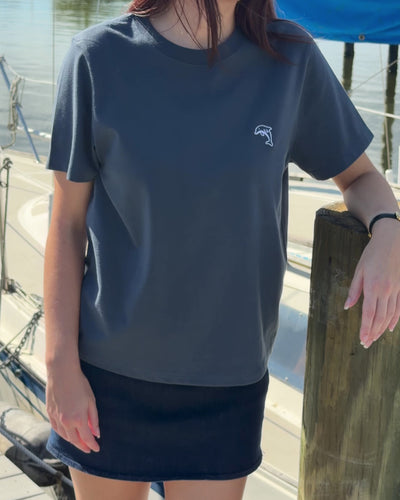 person wearing steel blue shirt with white dolphin logo and denim skirt on a boat dock