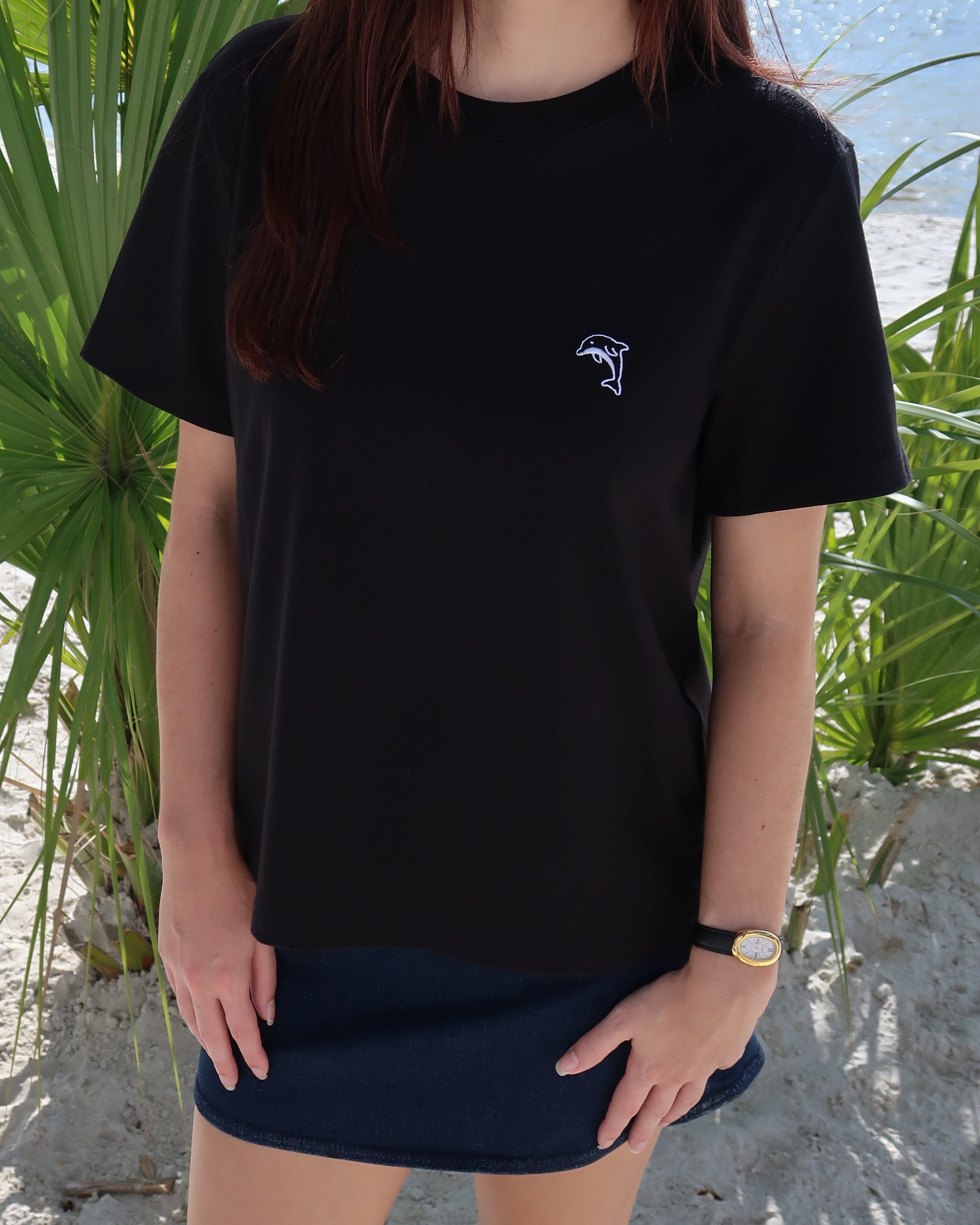 Person wearing a black t-shirt with a dolphin logo on a beach