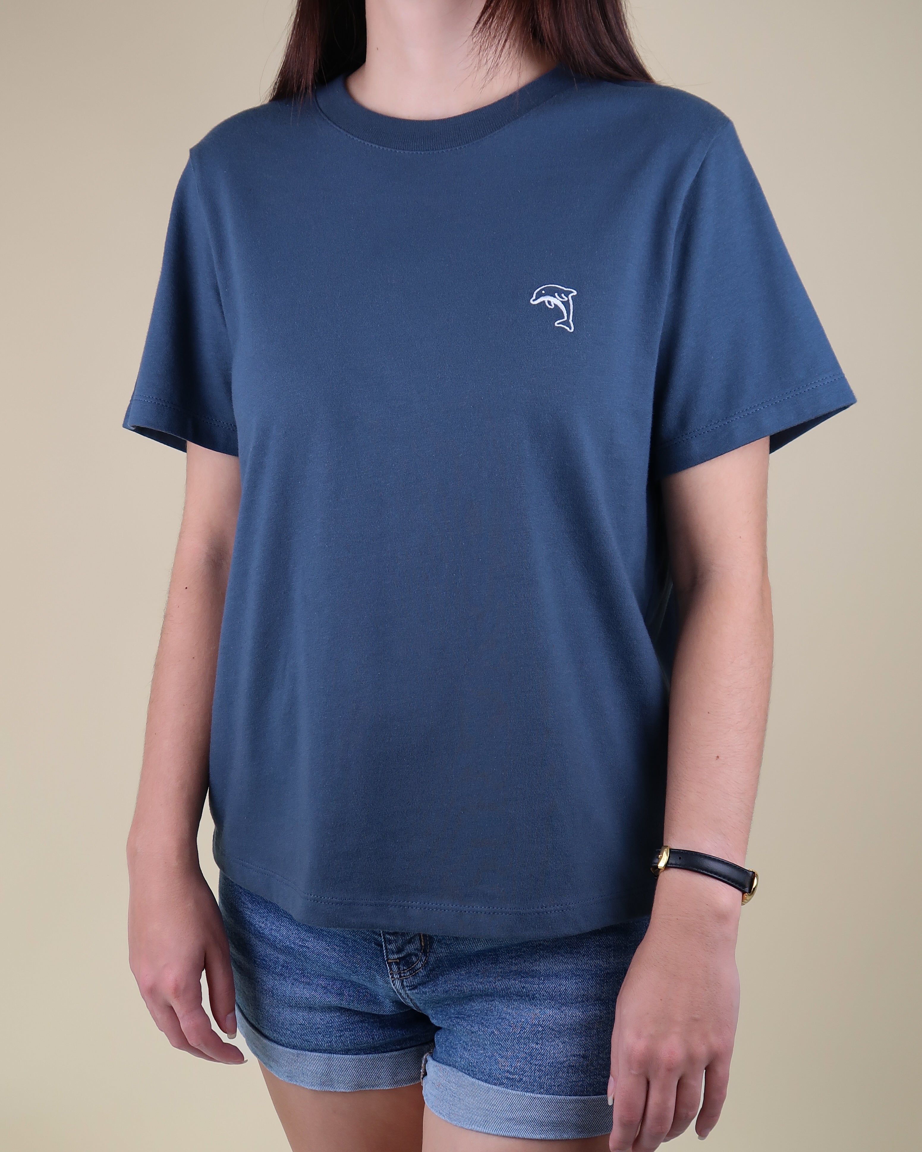 Person wearing a steel blue t-shirt with a dolphin logo on a beige background